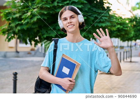 Smiling teenage male student with textbooks looking at camera outdoor Smiling teenage male student with textbooks looking at camera outdoor 90844690