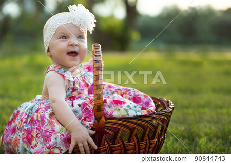 Happy little girl sits in a basket and laughs. A beautiful child. Little baby up to a year old on a summer meadow. Happy little girl sits in a basket and laughs. A beautiful child. Little baby up to a year old on a summer meadow. 90844743