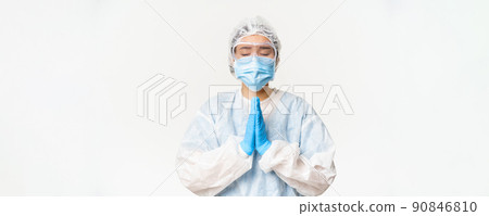 Hopeful asian female doctor or nurse in personal protective equipment and face mask, hoping, praying for smth, standing over white background 90846810