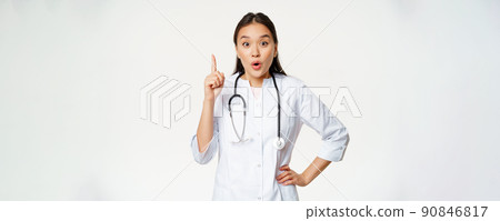 Healthcare and medical concept. Asian woman doctor raising finger, found solution, treatment for patient, pointing up and looking enthusiastic, white background 90846817