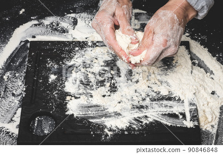 two female hands knead the dough from white wheat flour on a black table, top view two female hands knead the dough from white wheat flour on a black table, top view 90846848