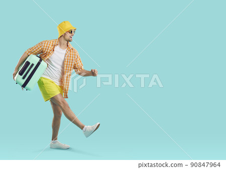 Happy excited guy tourist or vacationer, goes carrying travel suitcase on light blue background. 90847964