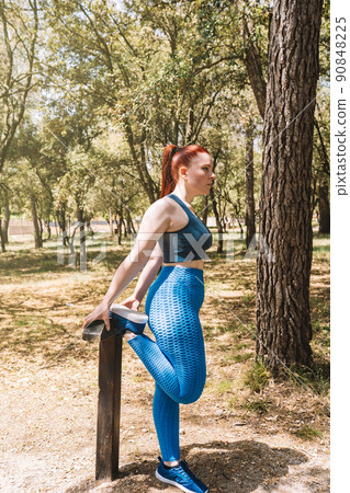 young woman practising leg stretches standing on a wooden bar outside. sportswoman preparing for a championship. health and wellness lifestyle. 90848225