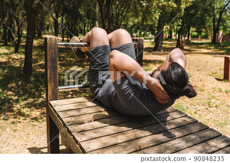 young athletic man doing abs in an outdoor public park. young athlete preparing for a championship. health and wellness lifestyle. young athletic man doing abs in an outdoor public park. young athlete preparing for a championship. health and wellness lifestyle. 90848235