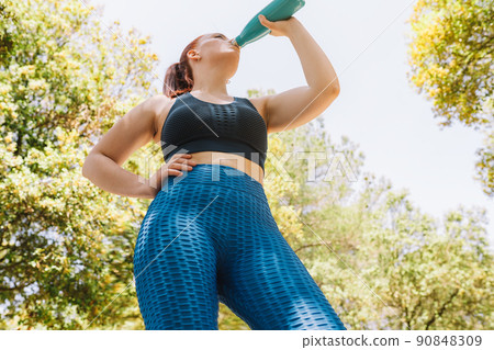 image from below of a young athlete drinking water to refresh herself from a bottle after a sports training. girl practising sport outdoors. health and wellness lifestyle. image from below of a young athlete drinking water to refresh herself from a bottle after a sports training. girl practising sport outdoors. health and wellness lifestyle. 90848309