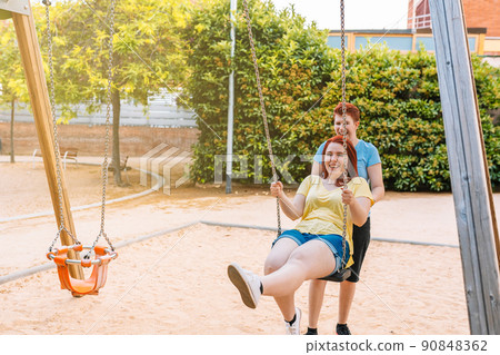 two young women laughing and playing like children in a public park with a swing. girls in the city. concept of friendship and companionship.ship. 90848362