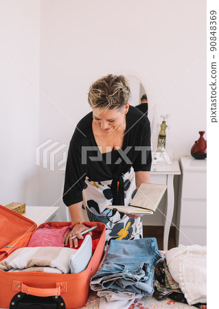 mature woman arriving at the hotel room and unpacking her luggage. summer trip, weekend. concept leisure and hobby. 90848369