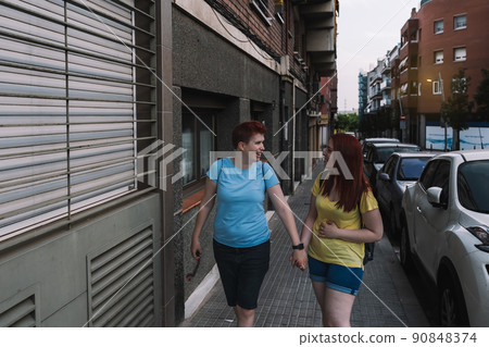 couple of young friends, happily walking home together on the city street at night. young girls in the city sharing free time while gossiping. concept of friendship and companionship. 90848374