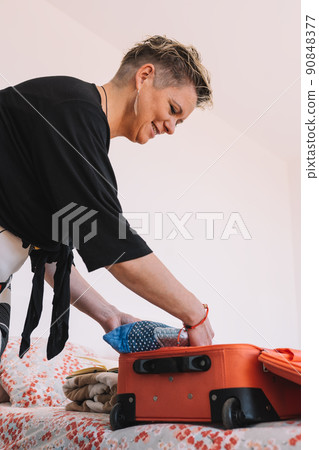 Blonde woman preparing luggage for her summer trip on the bed in the bedroom. Concept of leisure and holiday. 90848377