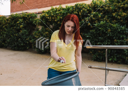 young woman recycling paper in a public waste bin in the city. responsible and environmentalist person. 90848385