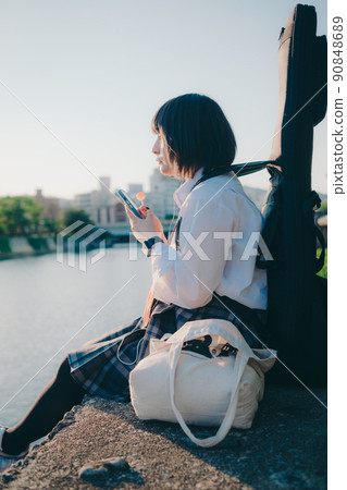 穿著制服的女學生有吉他和智能手機和城市 90848689