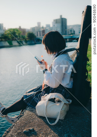 穿著制服的女學生有吉他和智能手機和城市 90848690