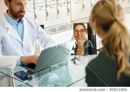 Woman looks in the mirror trying to choose glasses on the advice of an ophthalmologist 90851908