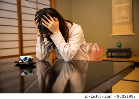 A woman holding her head at an inn worries 90851992