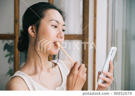 Women brushing their teeth while looking at their smartphones ・ Women using bamboo toothbrushes Women brushing their teeth while looking at their smartphones ・ Women using bamboo toothbrushes 90852079