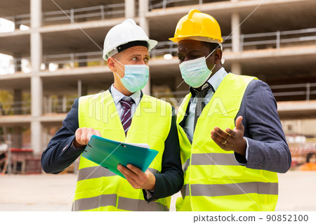 Portrait of an engineer and architect in protective mask with folder of documents at construction site Portrait of an engineer and architect in protective mask with folder of documents at construction site 90852100