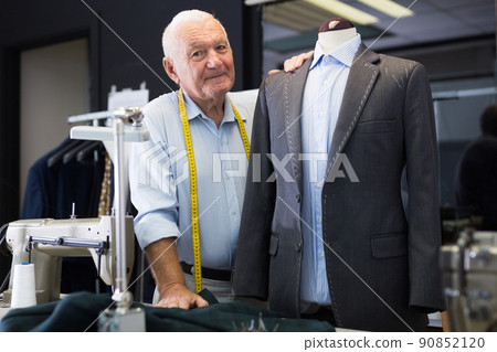 Experienced tailor threading jacket before starting work in workshop 90852120