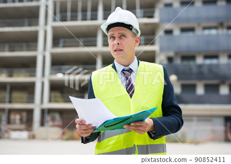 Architect in protective helmet and jacket with folder of documents on construction site Architect in protective helmet and jacket with folder of documents on construction site 90852411