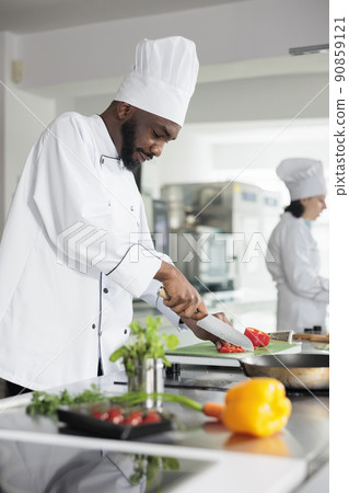 Food industry worker cutting fresh and organic vegetables while cooking gourmet dish for dinner service. Head chef in restaurant professional kitchen preparing delicious meal. 90859121