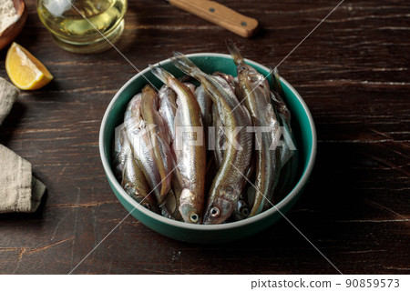 Fresh raw fish before cooking. A bowl of small fish, lemon and olive oil on a dark wooden table Fresh raw fish before cooking. A bowl of small fish, lemon and olive oil on a dark wooden table 90859573