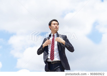 A business person who repairs the collar of his jacket with a serious expression under the blue sky 90860922