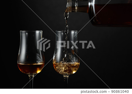 Strong alcohol drink is poured from a bottle into a glass. Strong alcohol drink is poured from a bottle into a glass. 90861040
