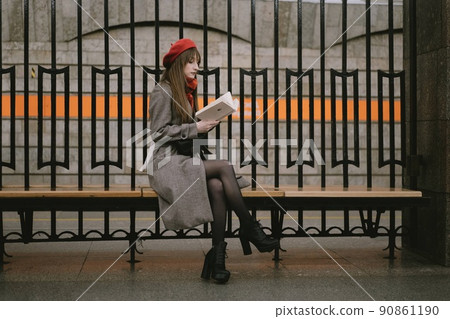 Beautiful Caucasian woman wearing coat, beret and scarf sitting alone on Saint Petersburg metro station reding a book. Image with selective focus and noise effect 90861190