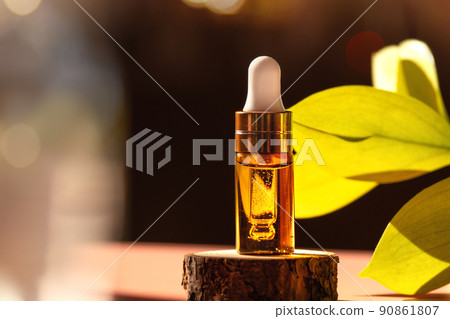Cosmetic amber glass dropper bottle on wooden podium with oil, serum or fruit peeling in the sunlight. Green ruscus, soft focus. Beauty product presentation, natural background. Front. Mockup concept  90861807