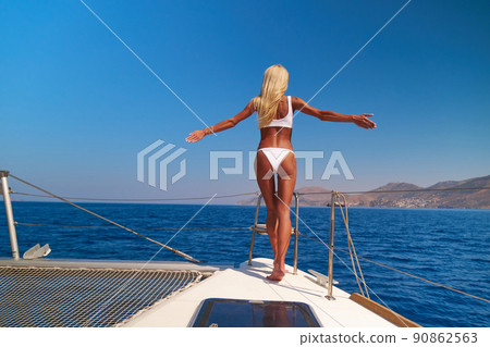 Beautiful young blond woman in bikini standing on yacht on the sea or ocean 90862563
