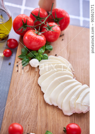 Ingredients for Caprese salad - sliced mozzarella cheese on wooden board, tomato and basil Ingredients for Caprese salad - sliced mozzarella cheese on wooden board, tomato and basil 90862571
