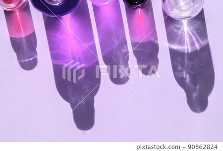 Different cosmetic glass bottles standing on violet background. Abstract pattern by shadows and illuminating reflections in the sunlight. Red, green and yellow shades. Flat lay style with copy space Different cosmetic glass bottles standing on violet background. Abstract pattern by shadows and illuminating reflections in the sunlight. Red, green and yellow shades. Flat lay style with copy space 90862824