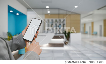 A female hand holding a mobile phone over blurred clinic or health care centre reception background. 90863308