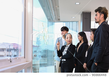 Confident skilled mature businesswoman explaining marketing data report financial results with company staff gathered at meeting 90866448