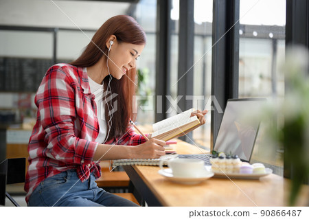 Asian female college student doing her homework, reading a textbook and listening online class. Asian female college student doing her homework, reading a textbook and listening online class. 90866487