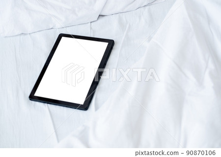 Digital life. Mobile mockup. Online connection. Tablet computer with blank screen laying bed in light room interior. Digital life. Mobile mockup. Online connection. Tablet computer with blank screen laying bed in light room interior. 90870106