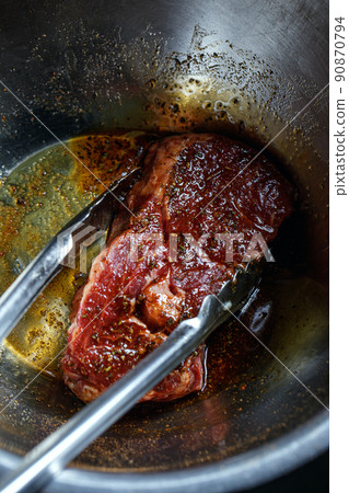 Silver serving kitchen tongs holding raw meat beef steak marinated and prepared for grilling on rack charcoal stove 90870794