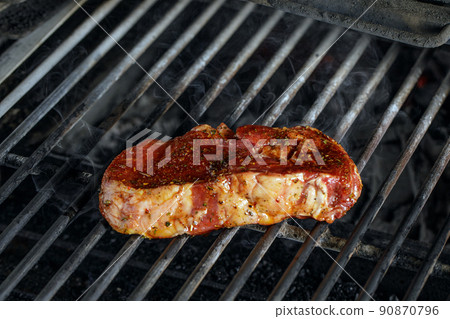 using silver serving kitchen tongs holding raw meat beef steak bbq grilling on rack charcoal stove with smoke on black background. 90870796