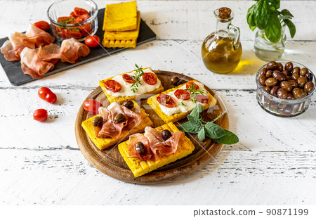 Grilled polenta with stracchino cheese, tomatoes, herbs, speck and olive. White wooden background, ingredients  90871199