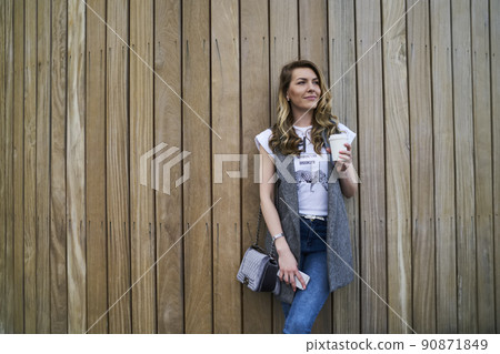 Young Caucasian woman with coffee to go smiling and thinking at promotional background 90871849