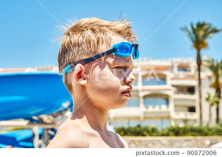 Serious schooler with goggles stands against hotel building 90872006
