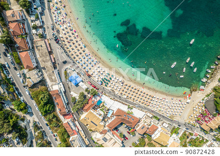 Beautiful colorful houses of seaside town, port of Parga with boats, cruise ship. Sand beach with umbrellas, tourist people, blue, turquoise sea water. Summer vacations and travel concept. Greece. 90872428