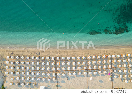 Aerial view of many white sunbed, lounge, umbrellas on sandy beach. Summer and travel concept. Blue, turquoise transparent water surface of ocean, sea, lagoon. Aerial, drone view 90872473