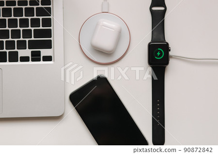 Working place with laptop on table and devices. Wireless charging of smart watch and wireless headphones on white table. Top view 90872842