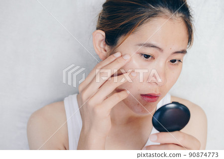 Portrait of Asian woman worry about her face when she saw the problem of acne and scar by the mini mirror. Conceptual shot of Acne & Problem Skin on female face. 90874773