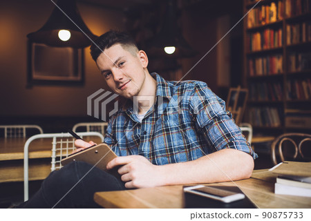 Positive man smiling and writing on clipboard at library 90875733