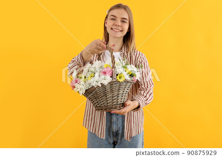 Attractive girl with basket of flowers on yellow background Attractive girl with basket of flowers on yellow background 90875929