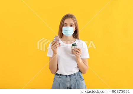 Sick girl in mask with pills on yellow background Sick girl in mask with pills on yellow background 90875931