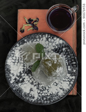 Green tea & Red bean daifuku with Butterfly pea tea over old book on dark background. Green tea & Red bean daifuku with Butterfly pea tea over old book on dark background. 90878458