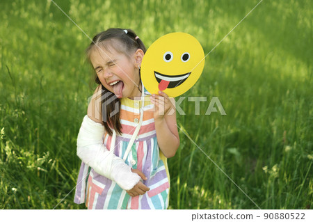 A bully child with a broken arm and a cast makes a grimace holding a smile face in his hand showing his tongue. A very emotional child. Emoji Day A bully child with a broken arm and a cast makes a grimace holding a smile face in his hand showing his tongue. A very emotional child. Emoji Day 90880522