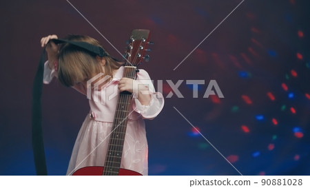 Cute little girl stands on stage in vintage dress and plays an acoustic guitar like a counter bass or cello. The concept of performing the author jazz and blues music. Hobbies and art among children Cute little girl stands on stage in vintage dress and plays an acoustic guitar like a counter bass or cello. The concept of performing the author jazz and blues music. Hobbies and art among children 90881028